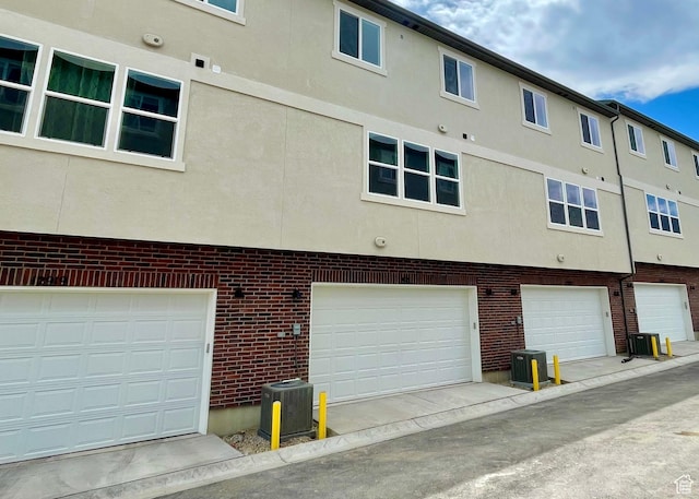 back of property with brick siding, central AC, stucco siding, and an attached garage