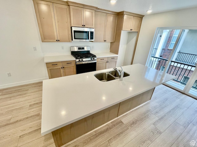 kitchen featuring a sink, light countertops, appliances with stainless steel finishes, a large island with sink, and light wood-style flooring