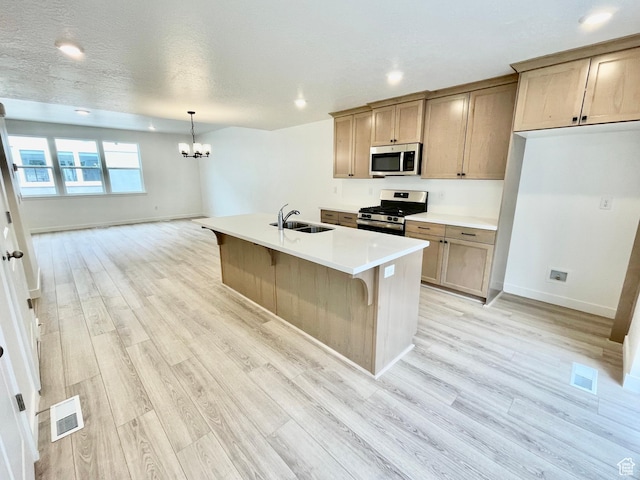 kitchen with a chandelier, a sink, light wood-style flooring, and stainless steel appliances