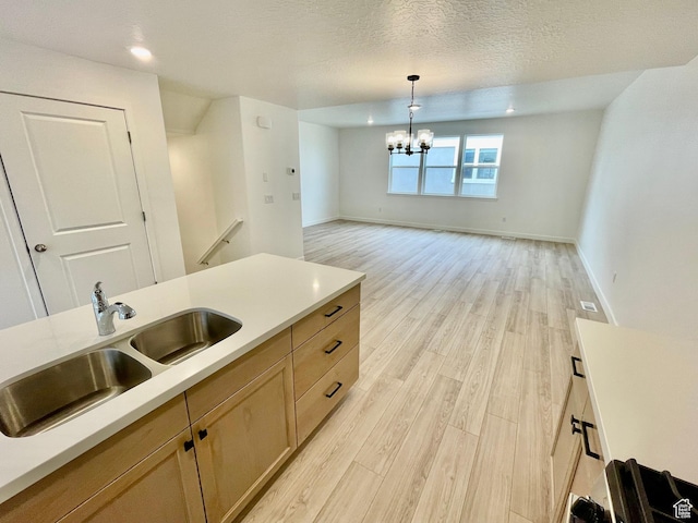 kitchen with light countertops, light wood-type flooring, a sink, and a notable chandelier