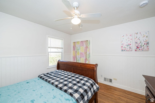 bedroom with baseboards, visible vents, wainscoting, ceiling fan, and wood finished floors