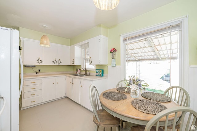 kitchen with light countertops, freestanding refrigerator, white cabinetry, decorative light fixtures, and a sink