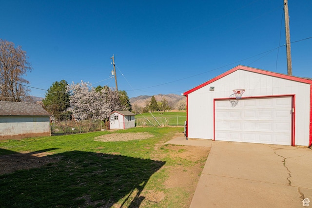 view of yard featuring an outbuilding, concrete driveway, a garage, and fence