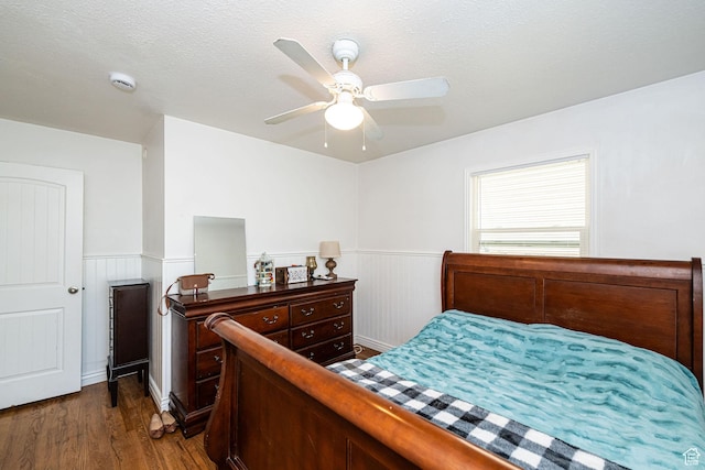 bedroom featuring a ceiling fan, dark wood finished floors, and a wainscoted wall