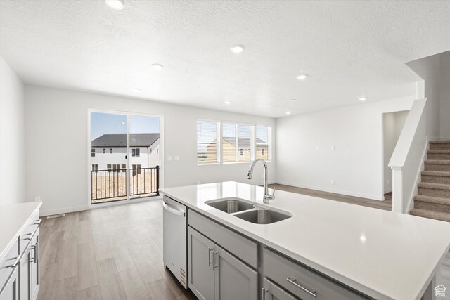 1345 N Harper Way Unit 0250, Tooele, UT 84074 - kitchen with stainless steel dishwasher, gray cabinetry, light wood finished floors, a kitchen island with sink, and light countertops