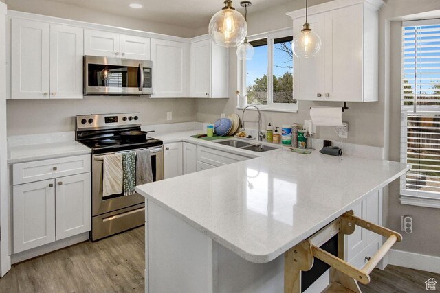 kitchen with light wood-type flooring, a peninsula, white cabinets, appliances with stainless steel finishes, and a sink