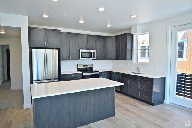 kitchen with light wood-style flooring, light countertops, a kitchen island, appliances with stainless steel finishes, and a sink