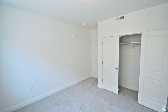 unfurnished bedroom featuring visible vents, a closet, baseboards, and light carpet