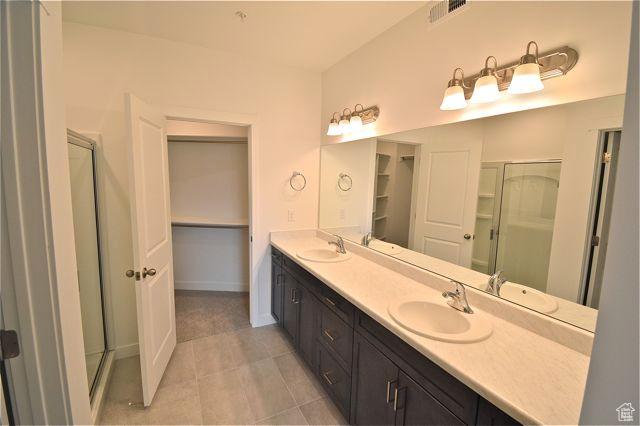 full bath featuring a shower stall, double vanity, visible vents, and a sink