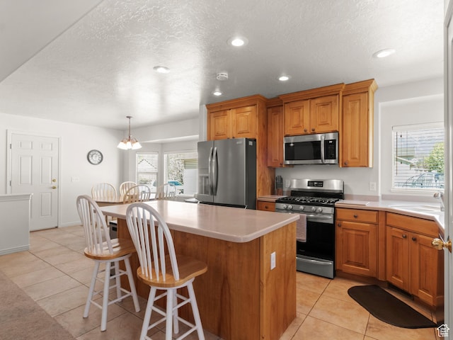 kitchen with a kitchen island, a sink, light tile patterned floors, and stainless steel appliances
