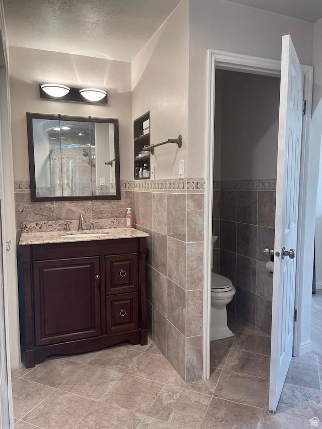 full bathroom with vanity, walk in shower, a wainscoted wall, toilet, and tile walls