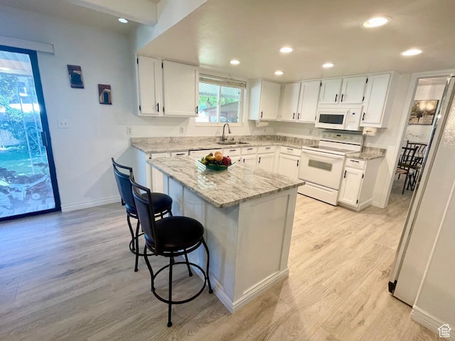 kitchen featuring light wood-style floors, white appliances, a kitchen breakfast bar, white cabinets, and a sink