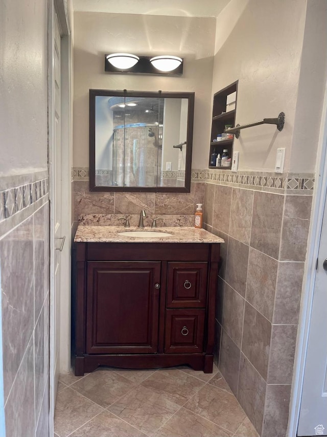 full bath featuring a shower stall, vanity, tile walls, and wainscoting