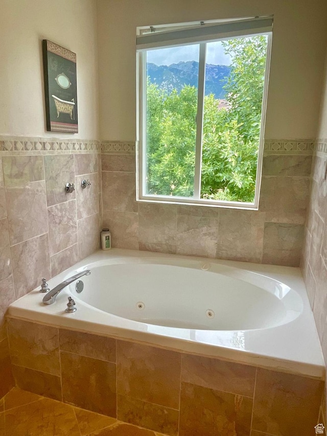 bathroom with a tub with jets, a wainscoted wall, and tile walls