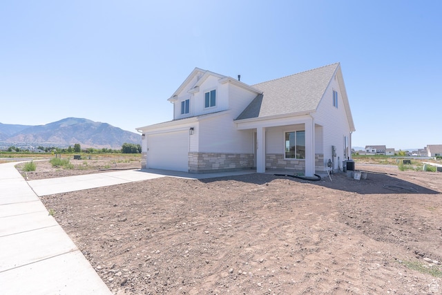 1038 W 2260 S Unit 105, Nibley, UT 84321 - view of side of property featuring driveway, a mountain view, an attached garage, stone siding, and roof with shingles
