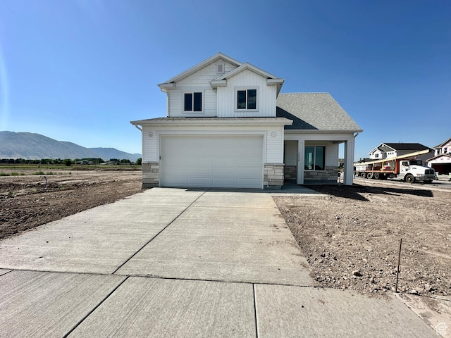 1038 W 2260 S Unit 105, Nibley, UT 84321 - view of front facade with driveway, a mountain view, stone siding, an attached garage, and covered porch