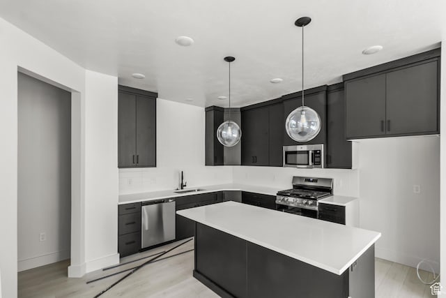 kitchen featuring a sink, appliances with stainless steel finishes, dark cabinets, light countertops, and hanging light fixtures