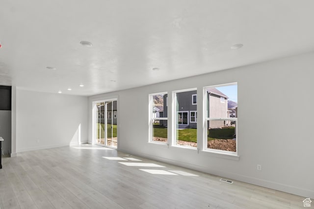 unfurnished living room featuring visible vents, plenty of natural light, baseboards, and light wood-style floors