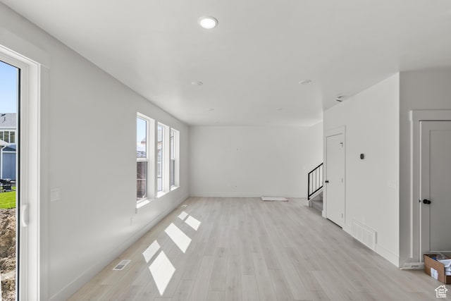unfurnished living room with baseboards, visible vents, stairs, and light wood-style flooring