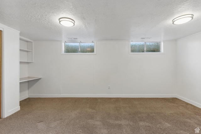 below grade area featuring built in features, a textured ceiling, carpet floors, a healthy amount of sunlight, and baseboards