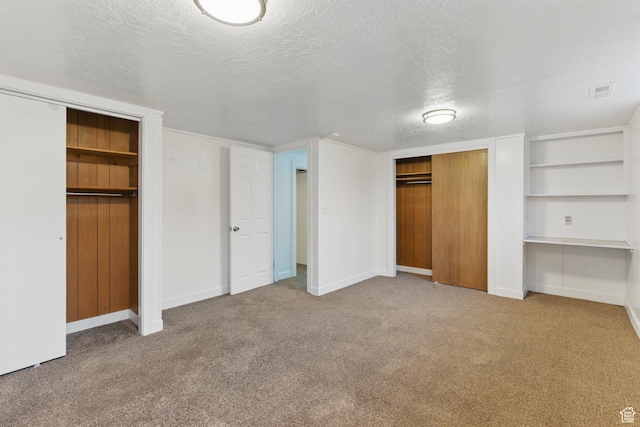 unfurnished bedroom with carpet flooring, a textured ceiling, and two closets