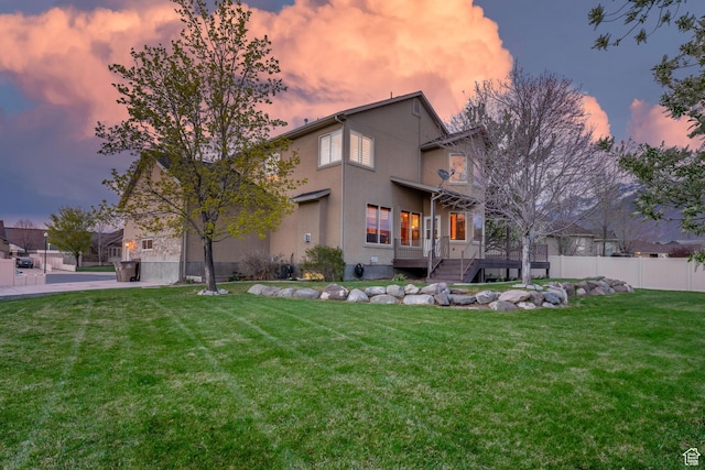 back of property with fence, a deck, a yard, and stucco siding