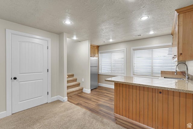 kitchen with a peninsula, a sink, stainless steel fridge, a textured ceiling, and baseboards