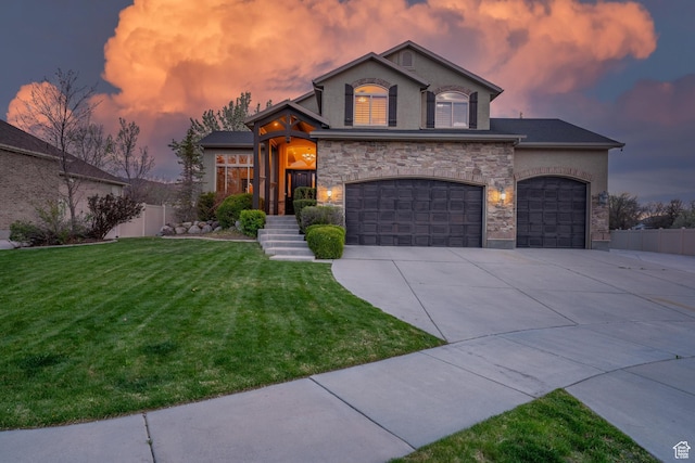 view of front of home featuring a lawn, driveway, stone siding, fence, and stucco siding