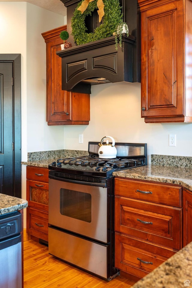 kitchen featuring light wood-style flooring, stainless steel gas stove, custom range hood, and light stone countertops