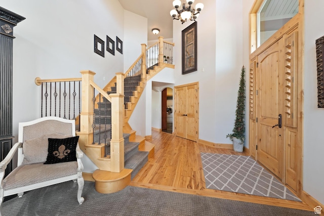 foyer entrance with wood finished floors, stairs, a towering ceiling, baseboards, and a notable chandelier