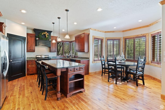 kitchen with light wood-type flooring, a kitchen island, appliances with stainless steel finishes, and baseboards