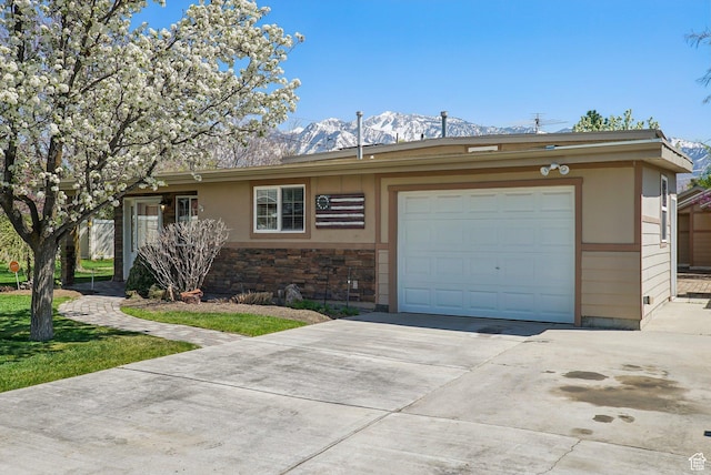 single story home featuring concrete driveway, stone siding, a mountain view, and a garage