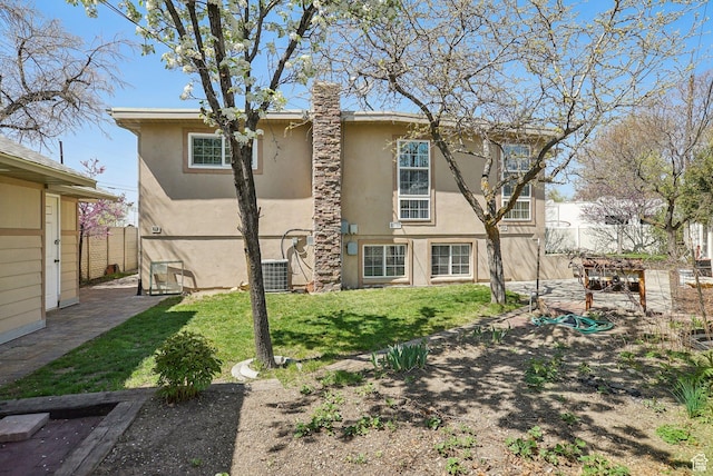 rear view of house featuring stucco siding, a chimney, central AC unit, a yard, and fence