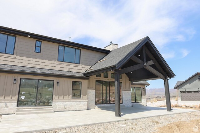 3896 N Eagle Ridge Dr Unit 61, Eden, UT 84310 - rear view of house featuring roof with shingles, stone siding, a chimney, board and batten siding, and a patio