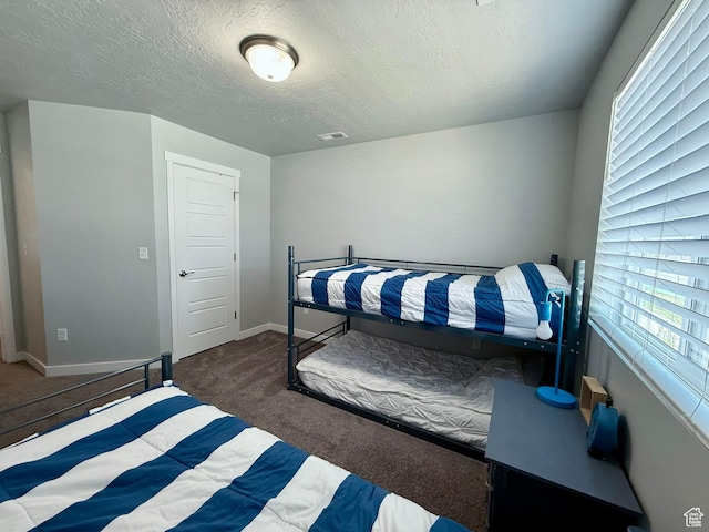carpeted bedroom featuring a textured ceiling, baseboards, multiple windows, and visible vents