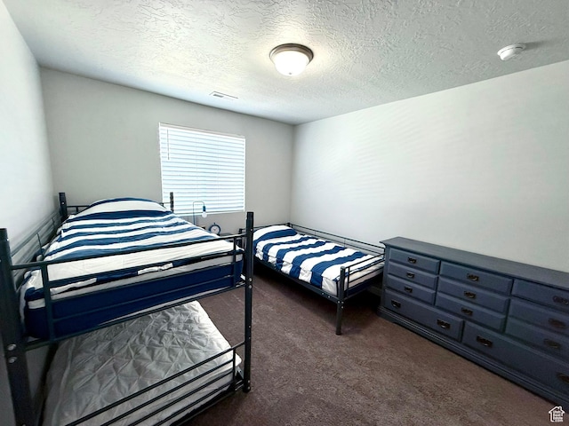 bedroom with dark carpet, visible vents, and a textured ceiling