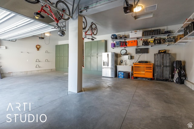 garage with stainless steel refrigerator with ice dispenser, visible vents, a sink, and a garage door opener