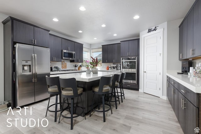 kitchen with light wood-type flooring, a breakfast bar, recessed lighting, and stainless steel appliances