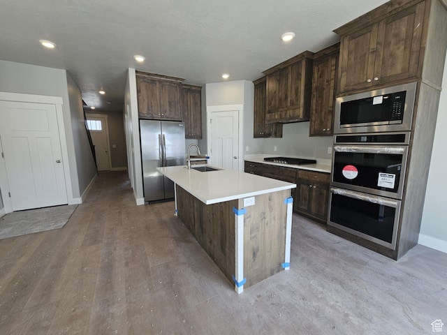 kitchen with light countertops, appliances with stainless steel finishes, a sink, and dark brown cabinetry