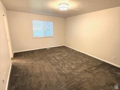spare room featuring a textured ceiling, baseboards, and dark colored carpet