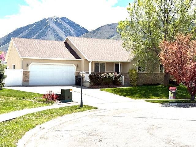 ranch-style home with an attached garage, driveway, a mountain view, and a front lawn