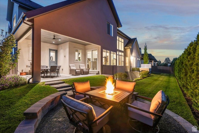 patio terrace at dusk with an outdoor living space with a fire pit, a yard, ceiling fan, and fence
