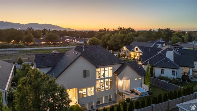 back of property at dusk with a mountain view, a fenced backyard, a residential view, and stucco siding