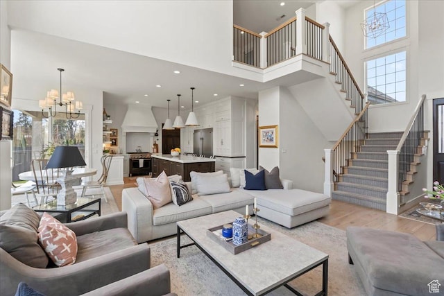 living area featuring a towering ceiling, a chandelier, a wealth of natural light, stairs, and light wood finished floors