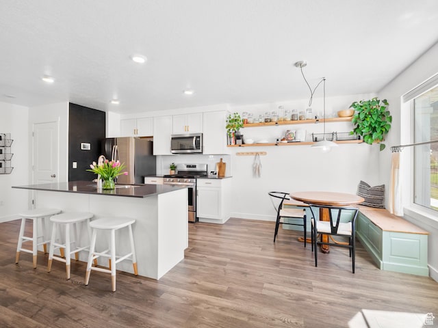 kitchen with light wood-style floors, open shelves, white cabinetry, appliances with stainless steel finishes, and dark countertops