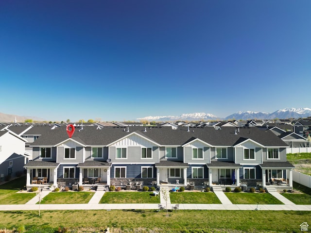 townhome / multi-family property featuring fence, stone siding, a front lawn, a mountain view, and a residential view