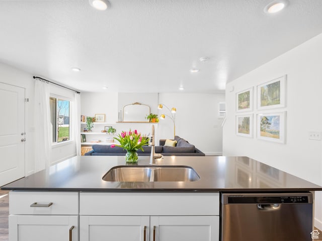 kitchen featuring white cabinets, dishwasher, a sink, open floor plan, and dark countertops