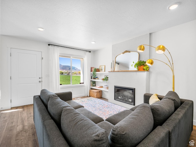 living area with baseboards, recessed lighting, a glass covered fireplace, and wood finished floors