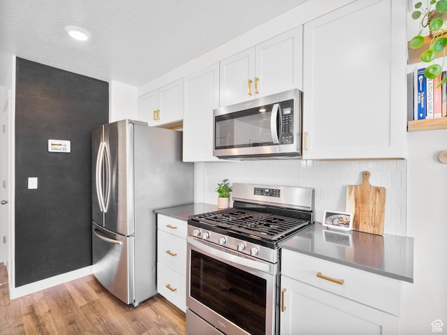 kitchen with tasteful backsplash, light wood-style flooring, dark countertops, white cabinets, and stainless steel appliances