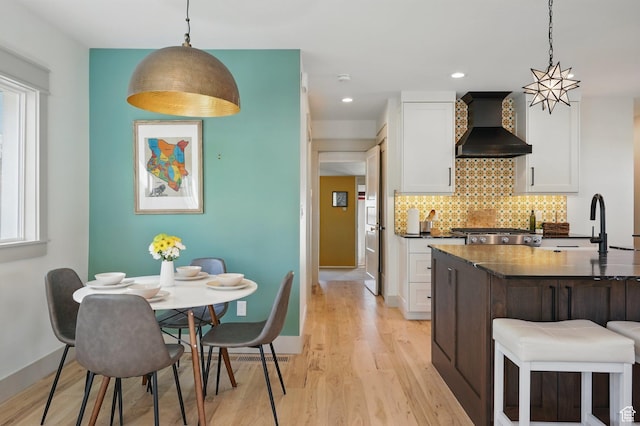 1148 E Kensington Ave, Salt Lake City, UT 84105 - kitchen with light wood-style floors, tasteful backsplash, wall chimney range hood, white cabinets, and a sink